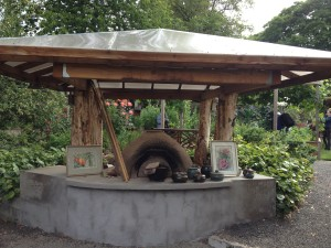 A covered outdoor area with a clay oven, art pieces, and pottery displayed on a concrete counter. 