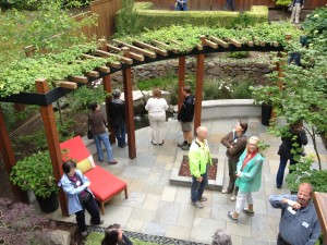 A patio with a curved pergola, plants, people, and a fire pit.