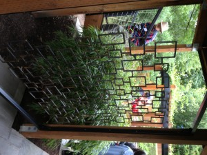 A metal screen with square cutouts, separating a walkway from a lush garden area. 