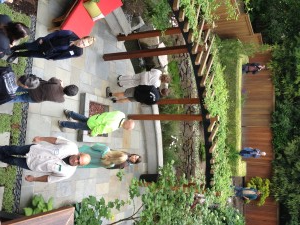 A patio with a pergola, water feature, and people viewing a landscaped garden.